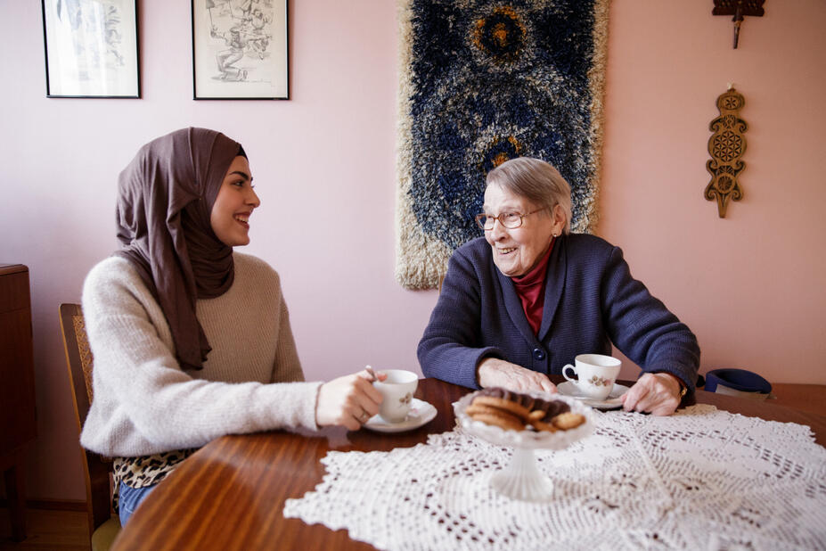 A younger and older woman are having a cup of coffee together at a table.