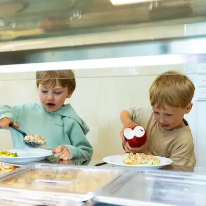 Two children at a daycare center getting food from the buffet line.
