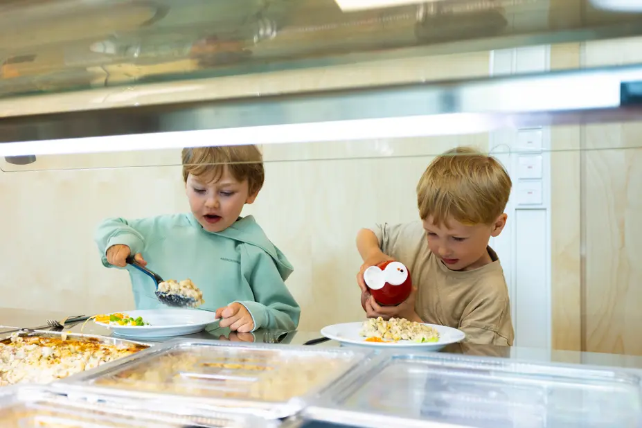 Two children at a daycare center getting food from the buffet line.